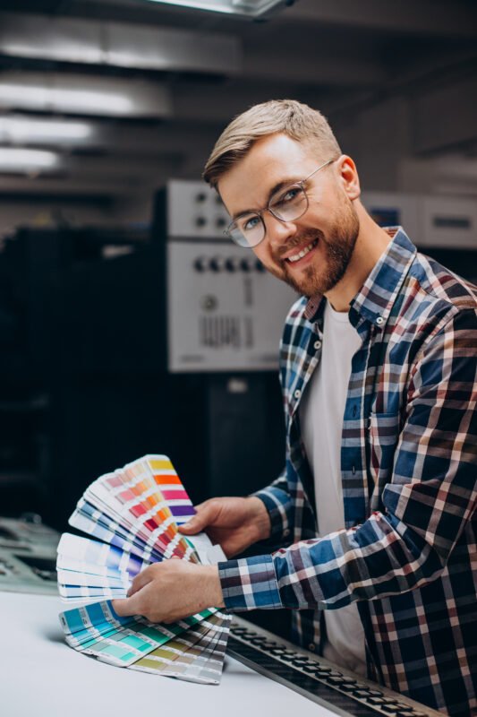 Man working in a printing house with paper sheets and paints.